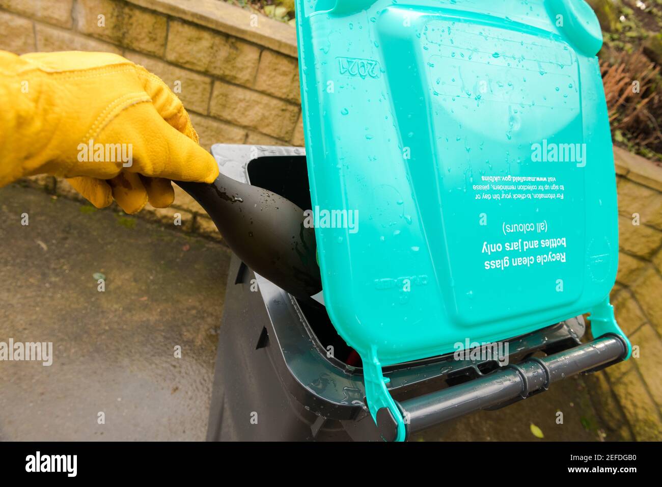 Person with yellow glove placing glass containers into a new glass recycling wheelie bin Stock