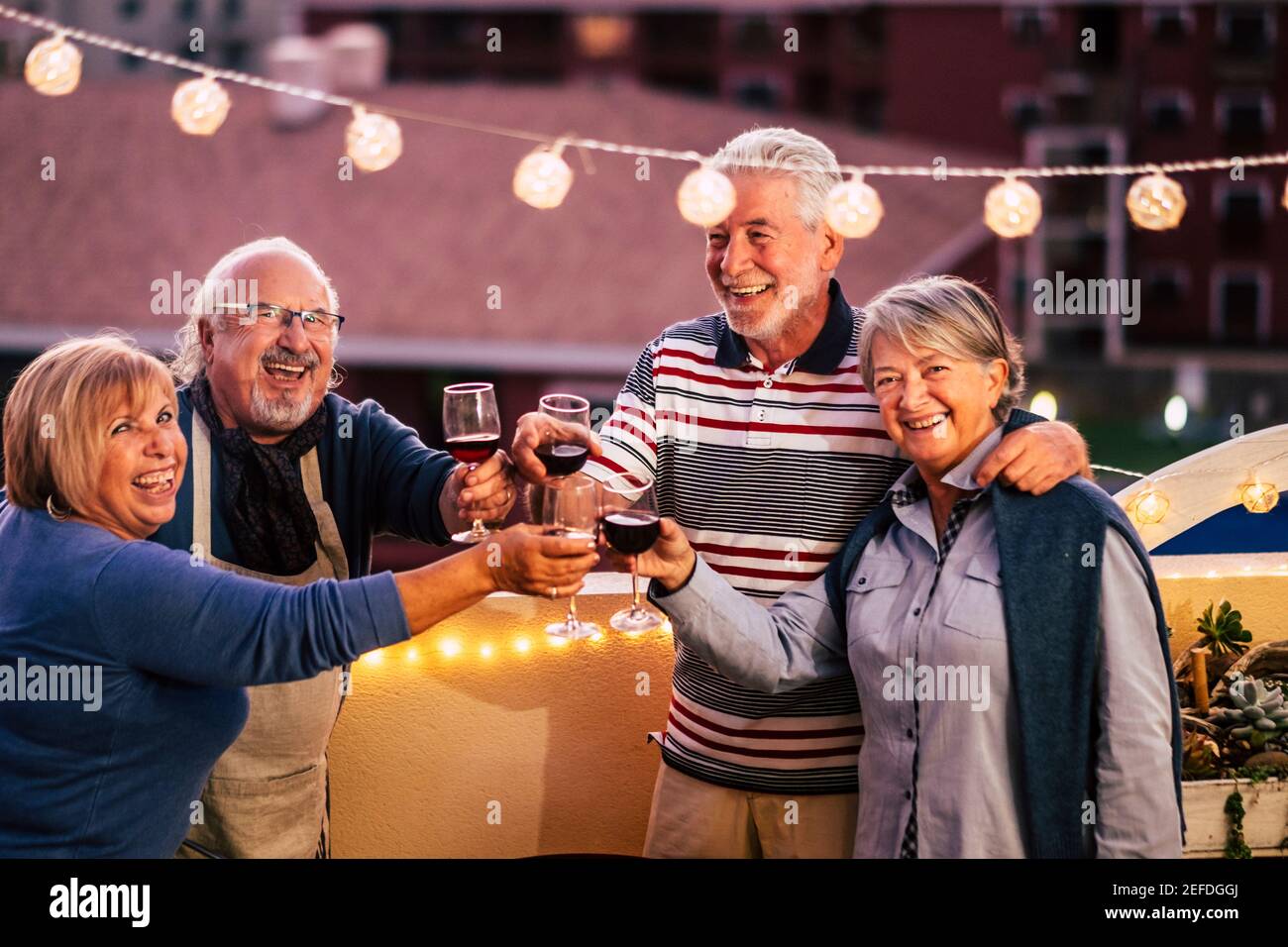 Happy group of old senior caucasian friends celebrate together by night clinking and toasting with red wine - end coronavirus emergency lokdown and pe Stock Photo
