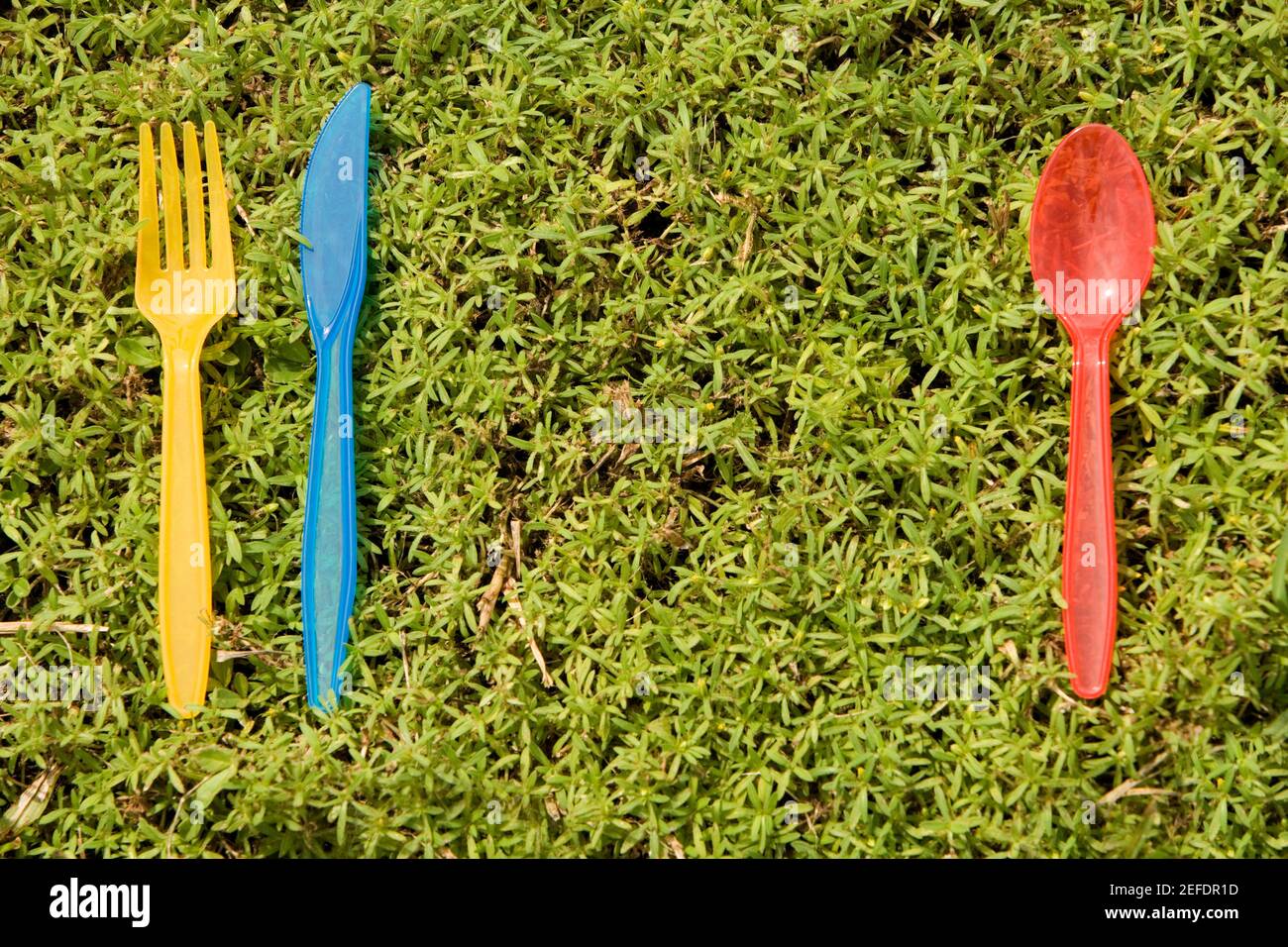 Close-up of a plastic spoon with a plastic knife and a plastic fork lying on the grass Stock Photo