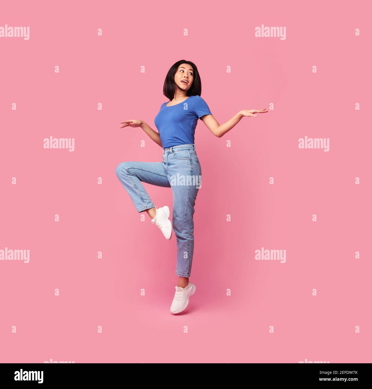 Having Fun. Full body length portrait of happy young asian woman jumping, dancing and looking aside at free space, being in a good mood, isolated over Stock Photo