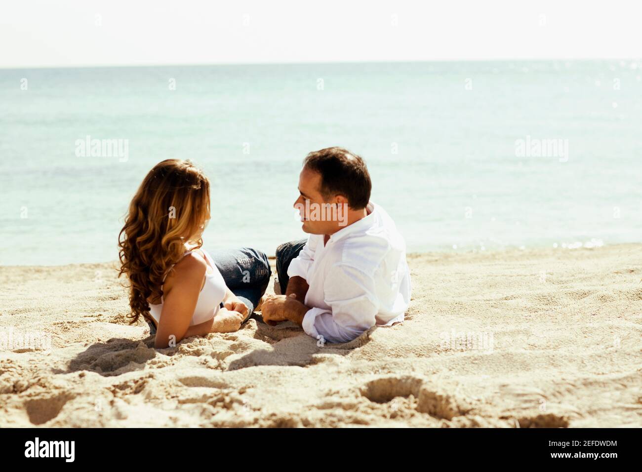 Side profile of a young woman and a mid adult man lying on the beach ...