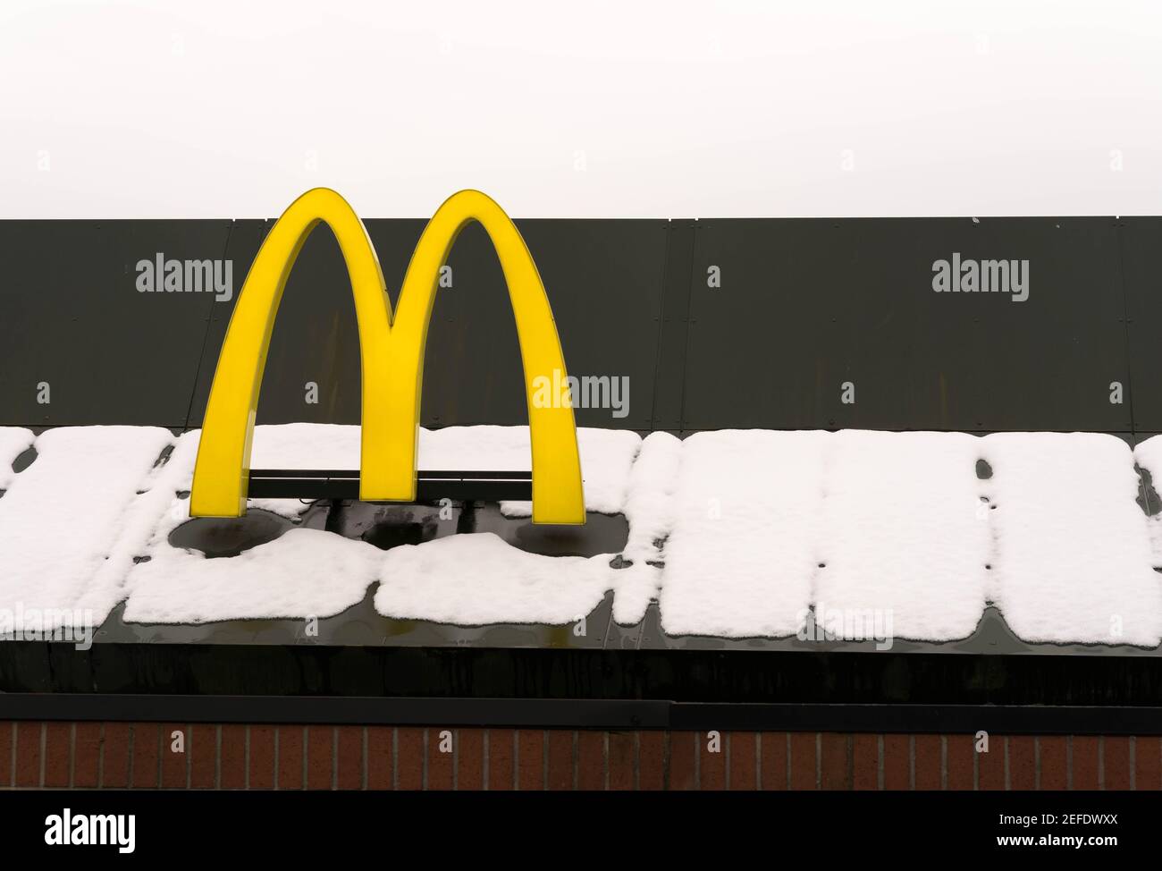 McDonalds M logo in yellow erected on tiled roof covered in white snow Sevenoaks Kent England Stock Photo