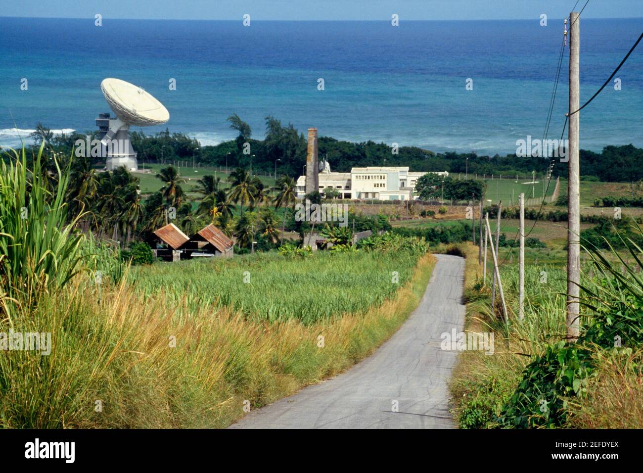 A road passing through lush meadows with a satellite dish at a side, Barbados, Caribbean Stock Photo