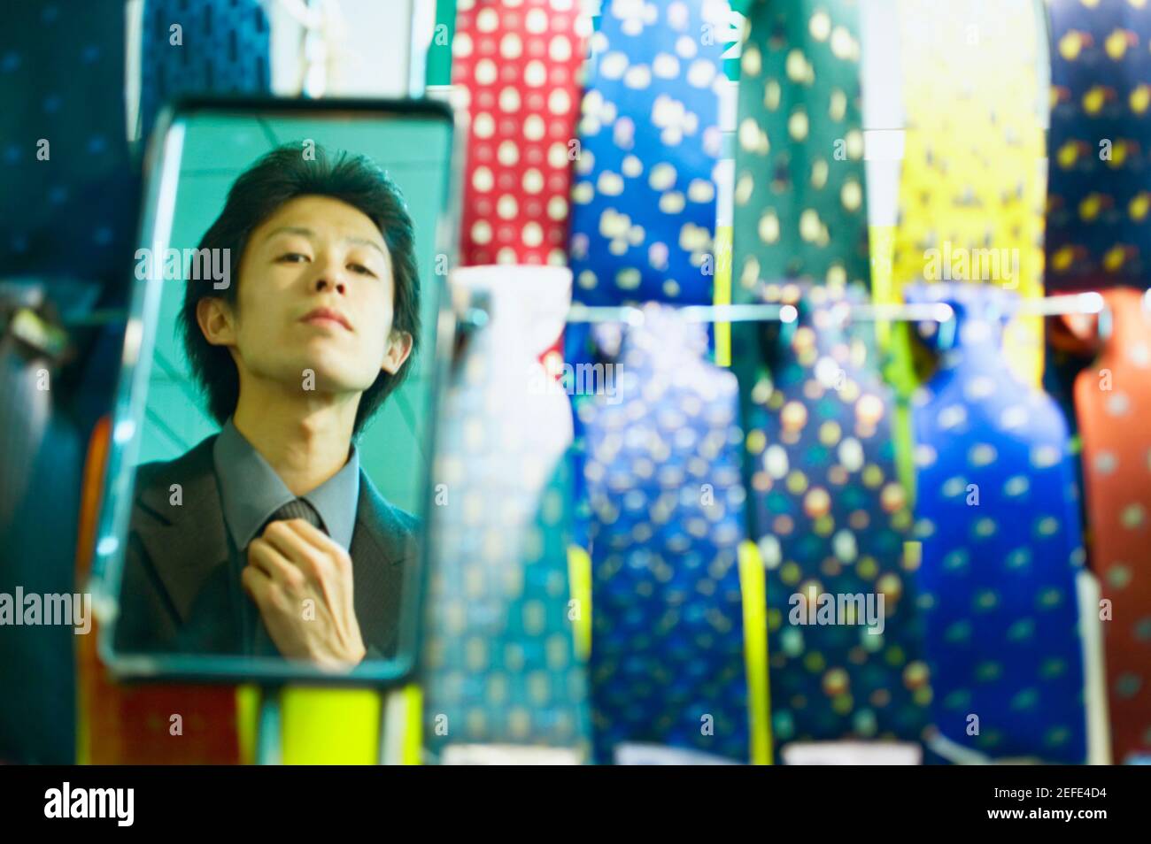 Reflection of a young man adjusting his tie in the mirror of a tie shop ...