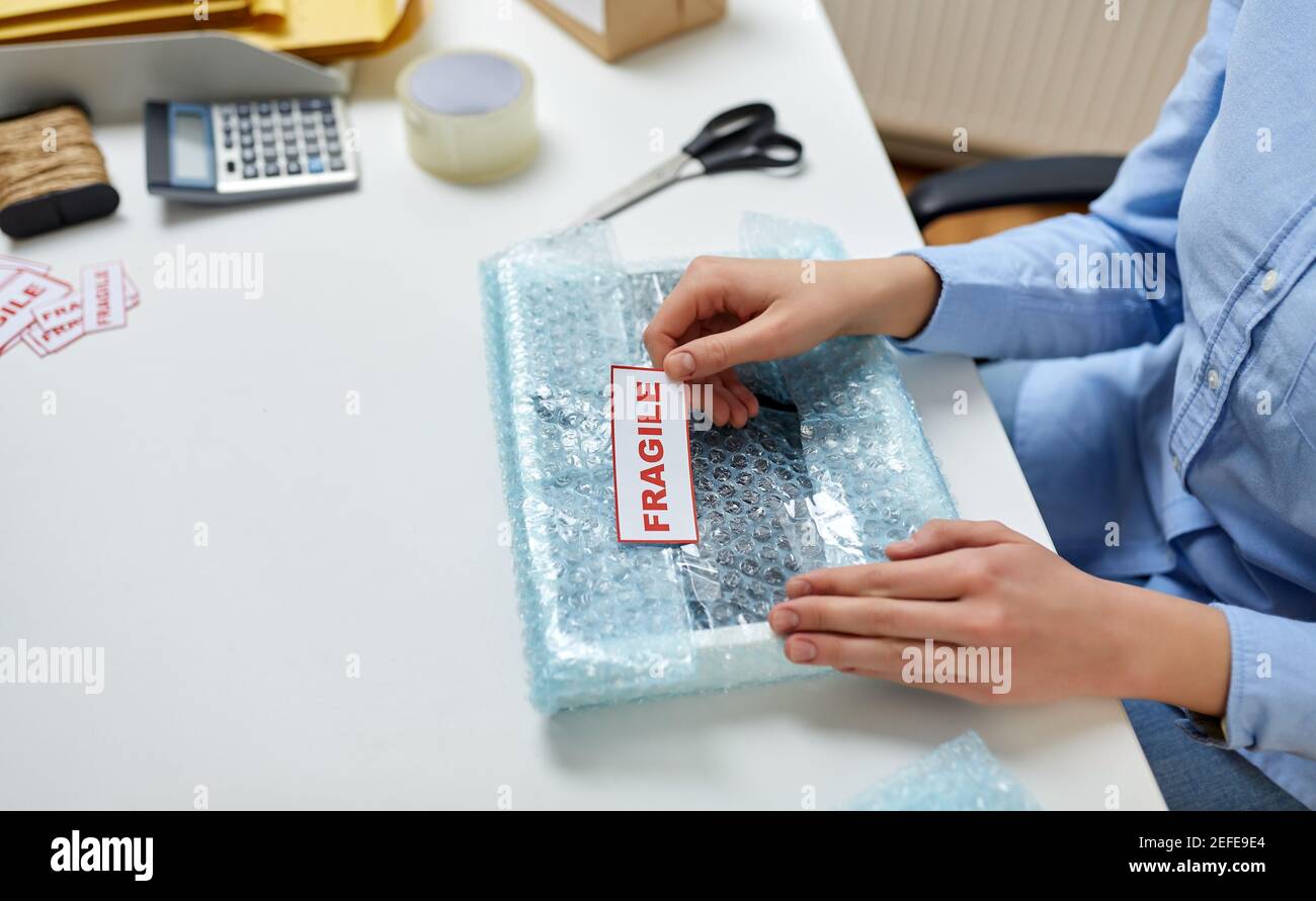 woman sticking fragile mark to wrap at post office Stock Photo