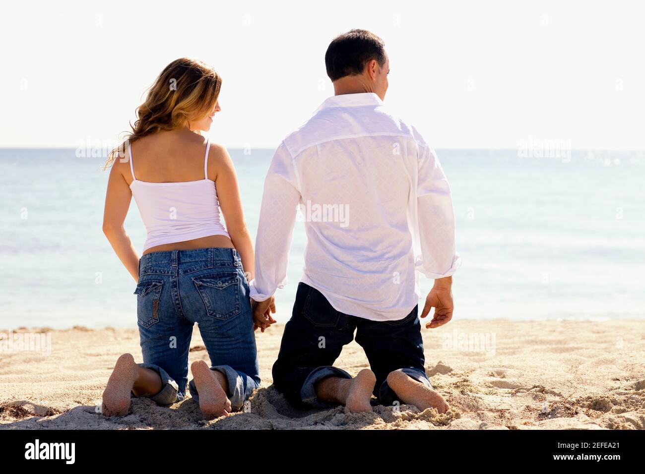 Rear view of a mid adult man and a young woman kneeling with holding ...