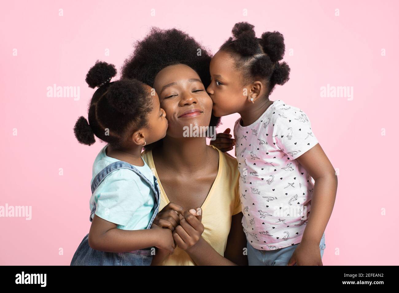 Motherhood and family concept. Lovely cute two little African girls kids in summer outfits, having fun and kissing their happy smiling young pretty Stock Photo