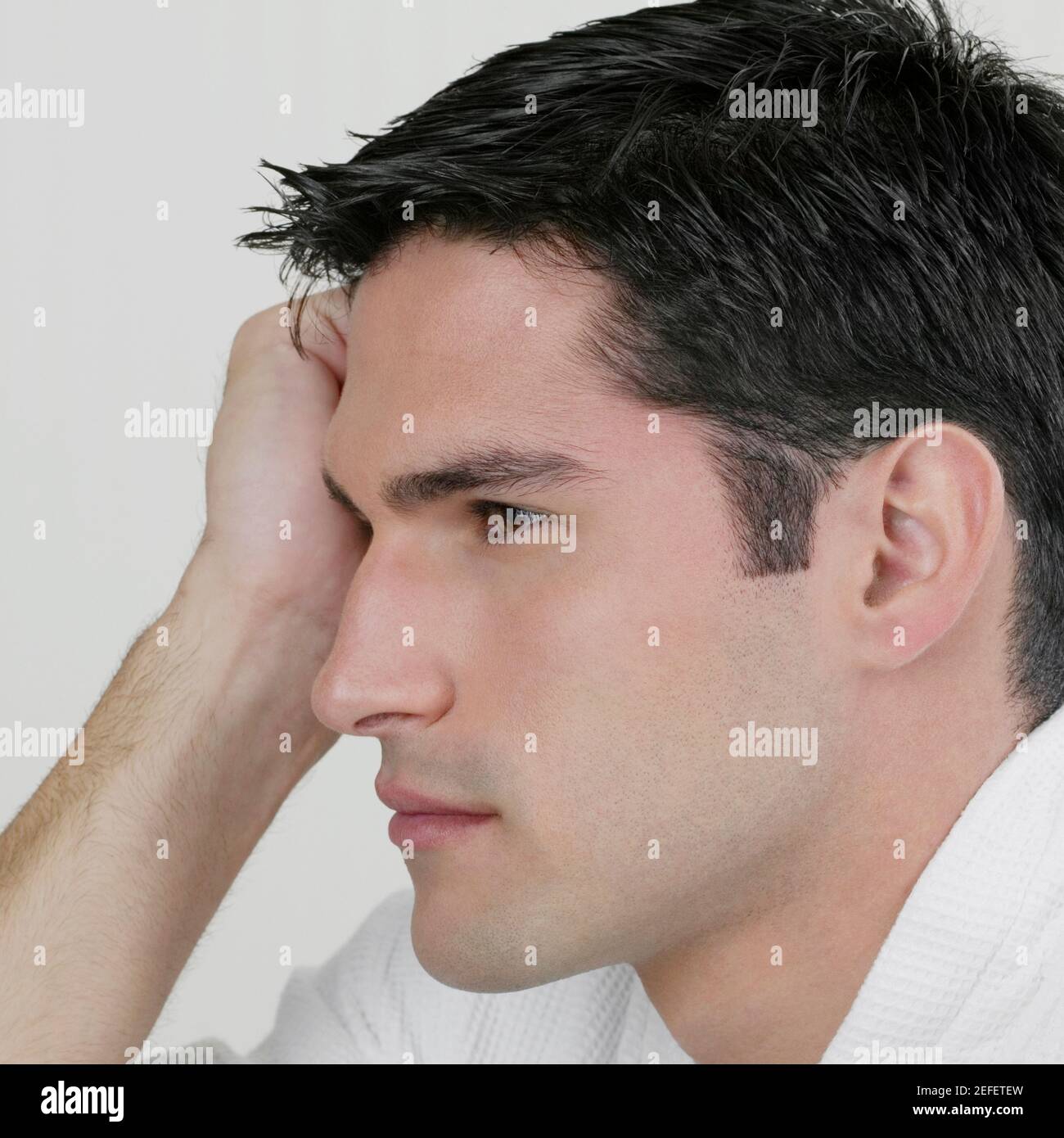 Side profile of a young man thinking with his head in his hand Stock Photo