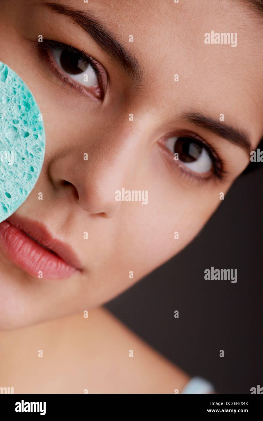 Portrait of a young woman scrubbing her face with a sponge Stock Photo