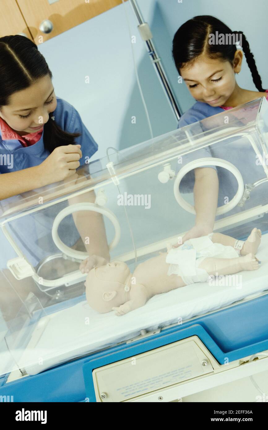 Two girls touching a doll in an incubator Stock Photo