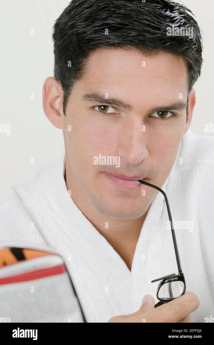 Portrait of a young man biting the shaft of his eyeglasses Stock Photo