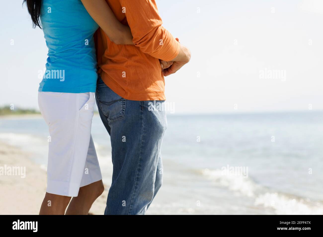 Mid section view of a woman embracing a man from behind on the beach ...