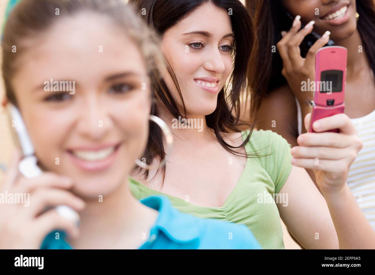 Teenage girl looking at a mobile phone with two other teenage girls talking on mobile phones Stock Photo