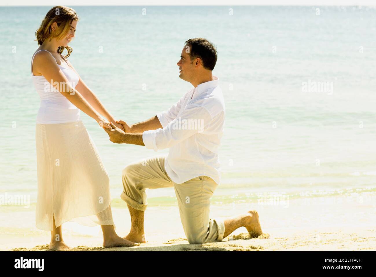 Side profile of a mid adult man kneeling in front of a young woman on ...