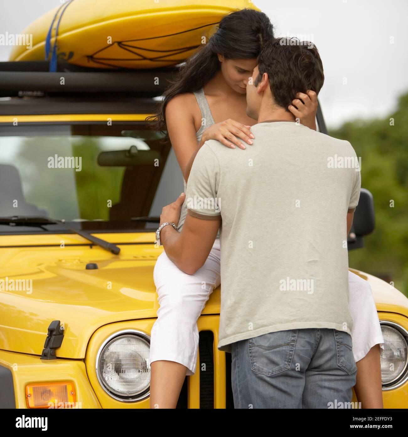 Mid adult man embracing a young woman sitting on the bonnet of a jeep ...