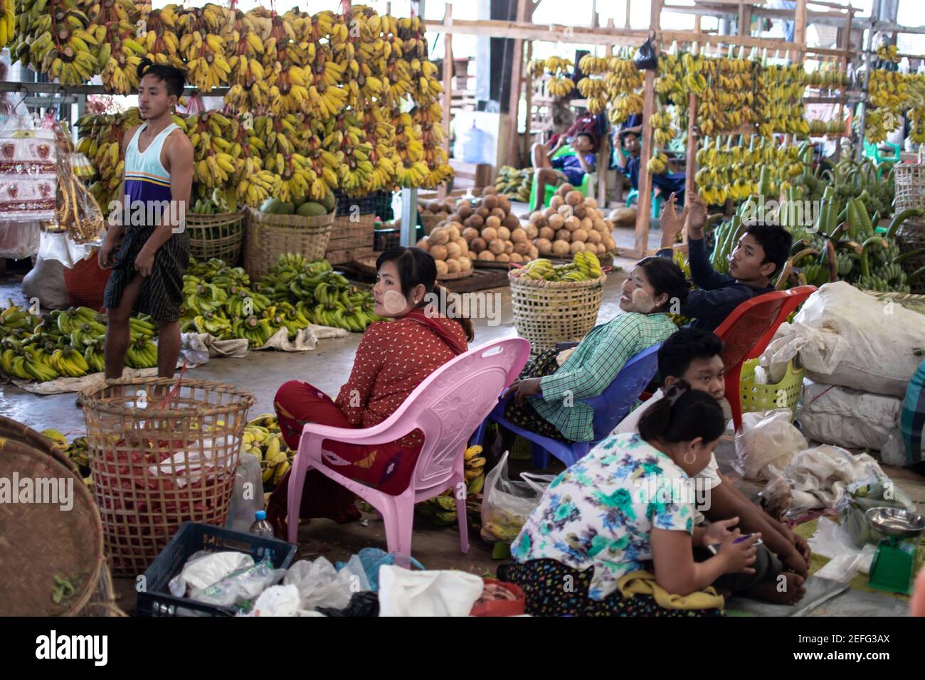 YANGON, MYANMAR - DECEMEBER 31 2019: Local Burmese people attending a street market by plenty of bananas and coconuts Stock Photo