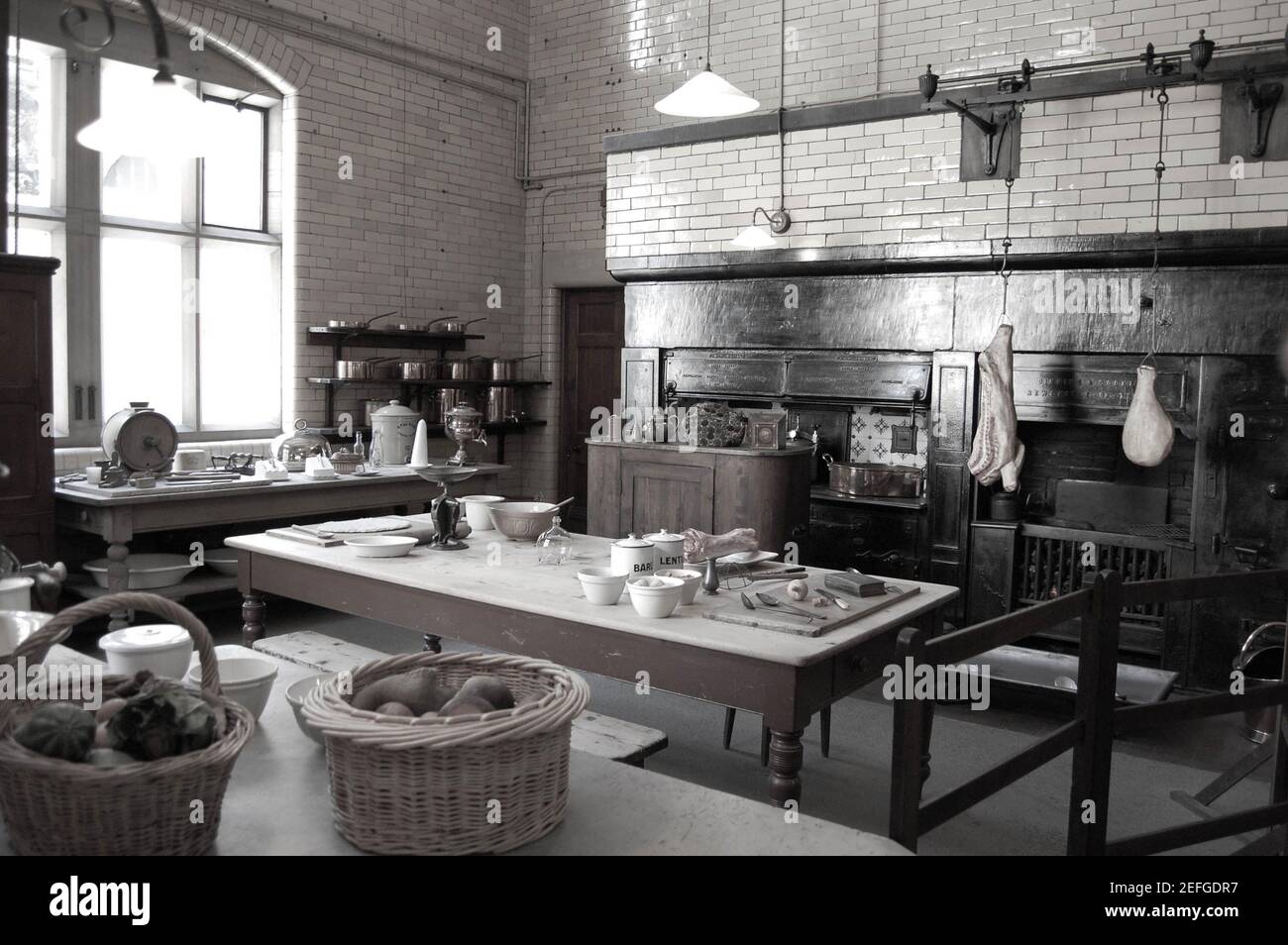 Cragside kitchen table meat hanging tiles fruit plates fireplace light lights basket baskets pots pans pot pan tables heater vegetables cooking Stock Photo