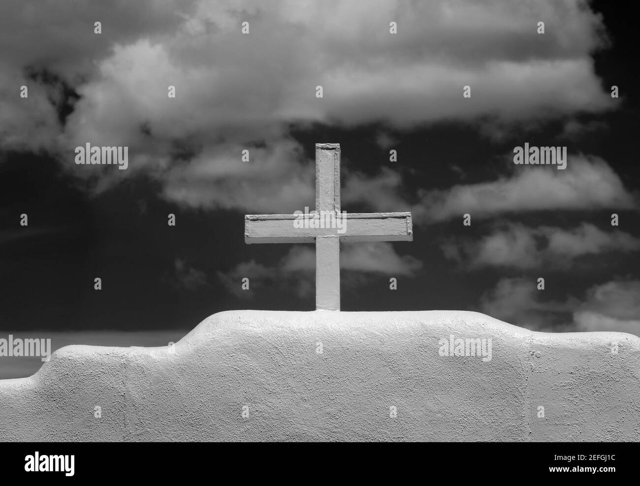 A Christian cross stands atop an adobe wall surrounding St. Jerome Chapel near Taos, New Mexico USA. Stock Photo