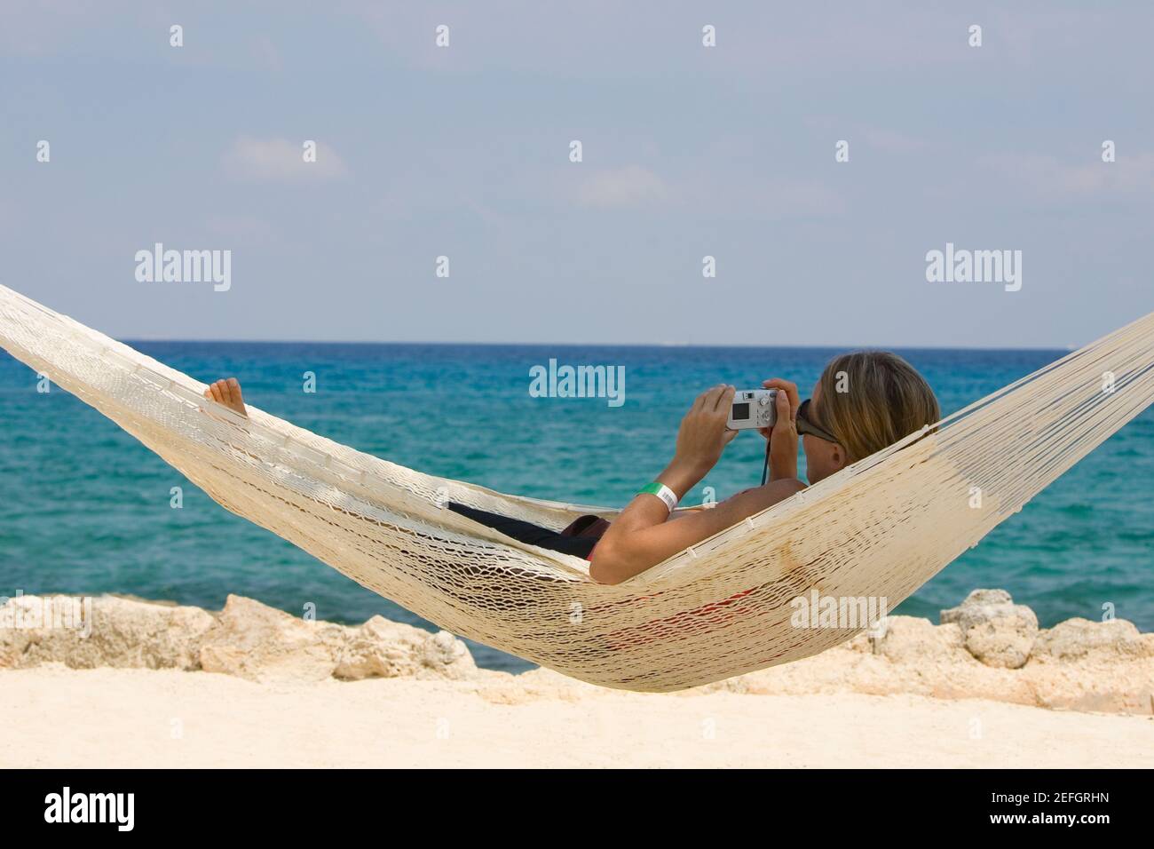 Young woman lying in a hammock and holding a digital camera, Cancun, Mexico Stock Photo