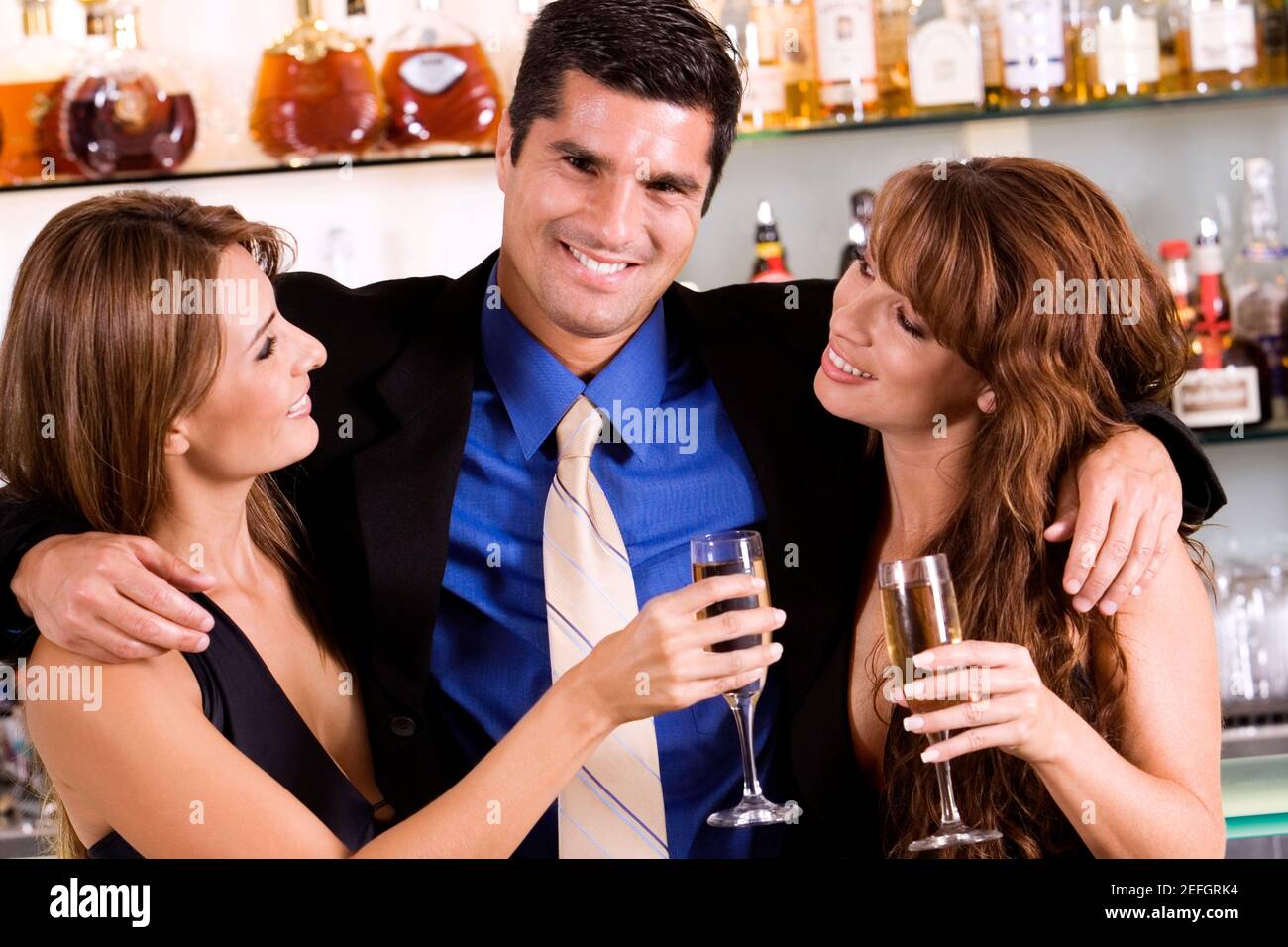 Portrait of a businessman with his arms around a young woman and a mid adult woman Stock Photo