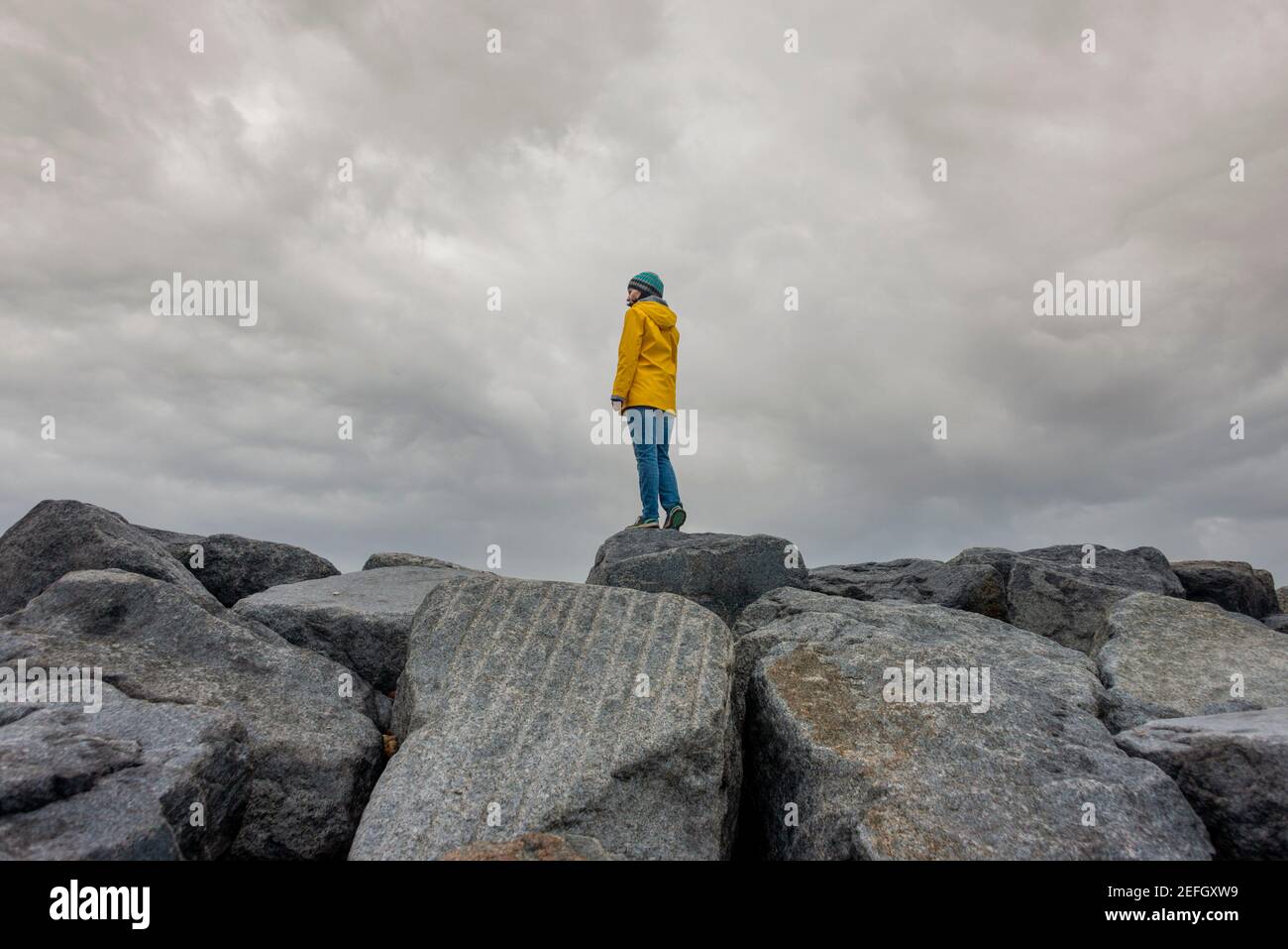 Woman wearing a yellow jacket standing on top of rocks. Away from it all. Stock Photo