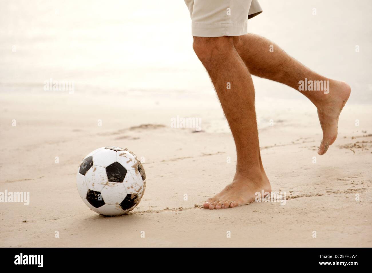 Low section view of a mid adult man playing soccer on the beach Stock Photo