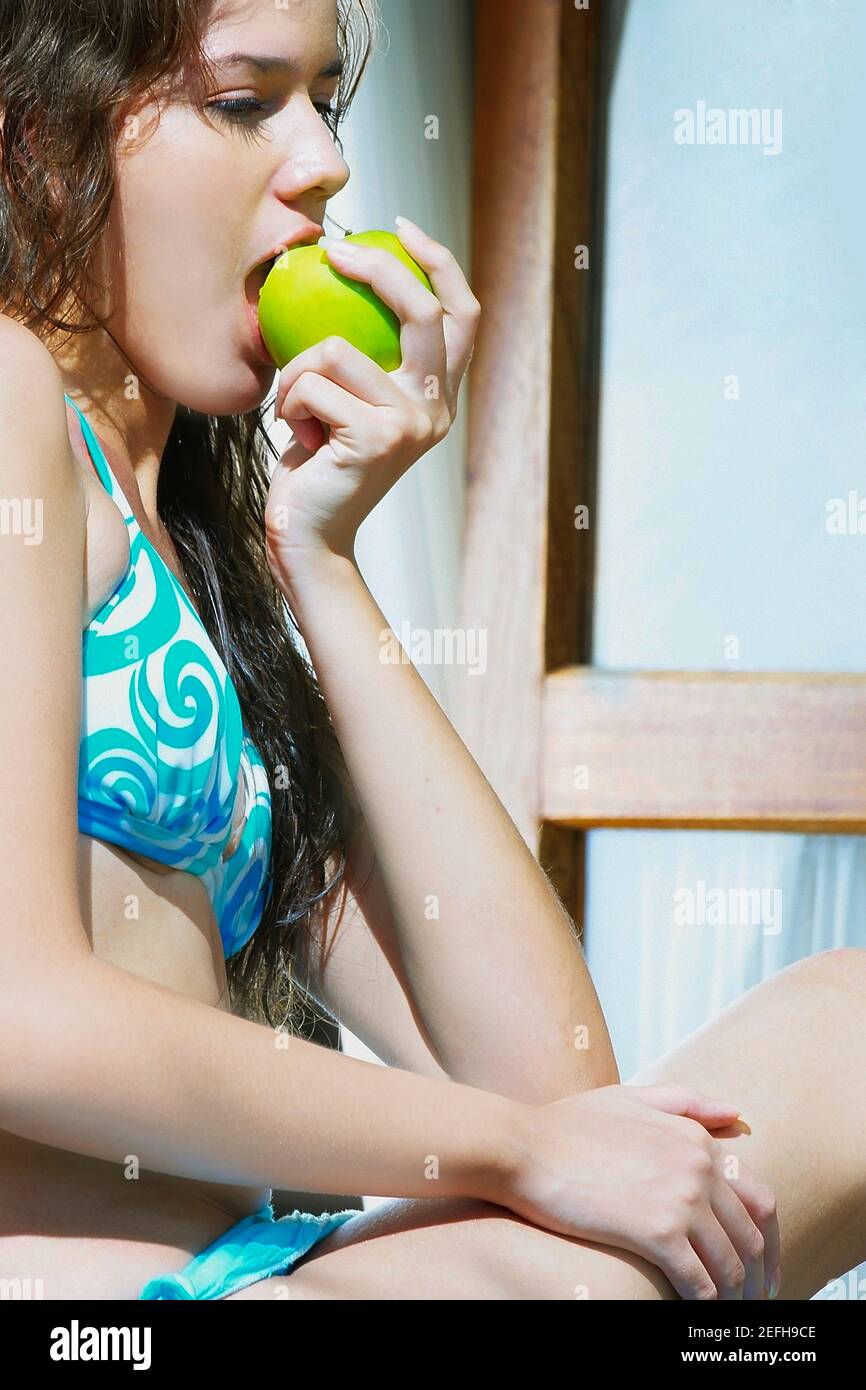 Side profile of a young woman eating a green apple Stock Photo
