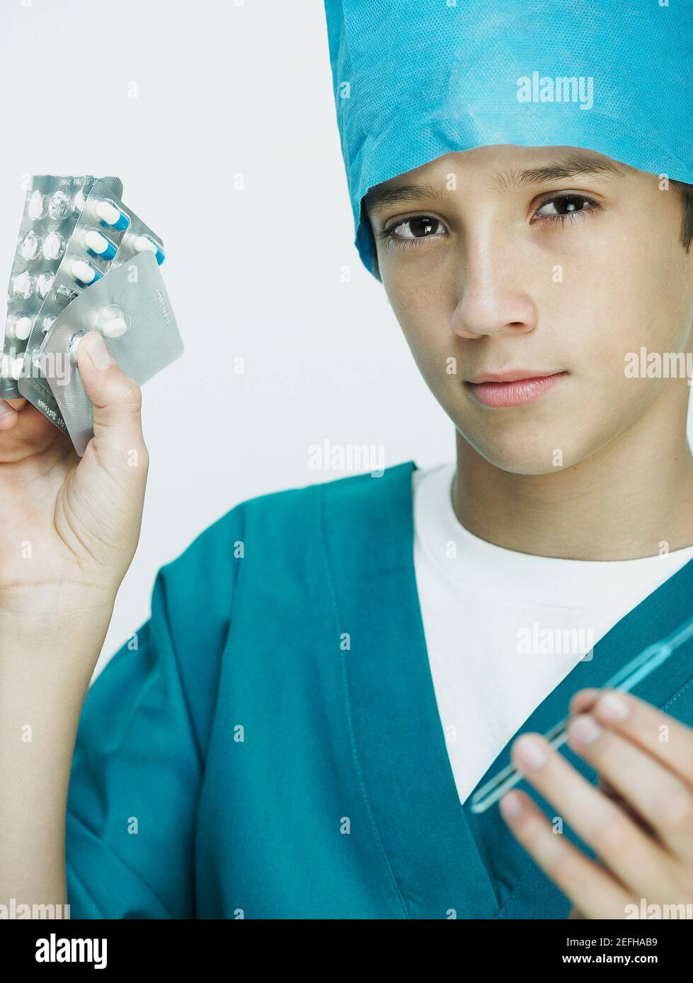 Portrait of a boy wearing surgical scrubs and holding blister packs