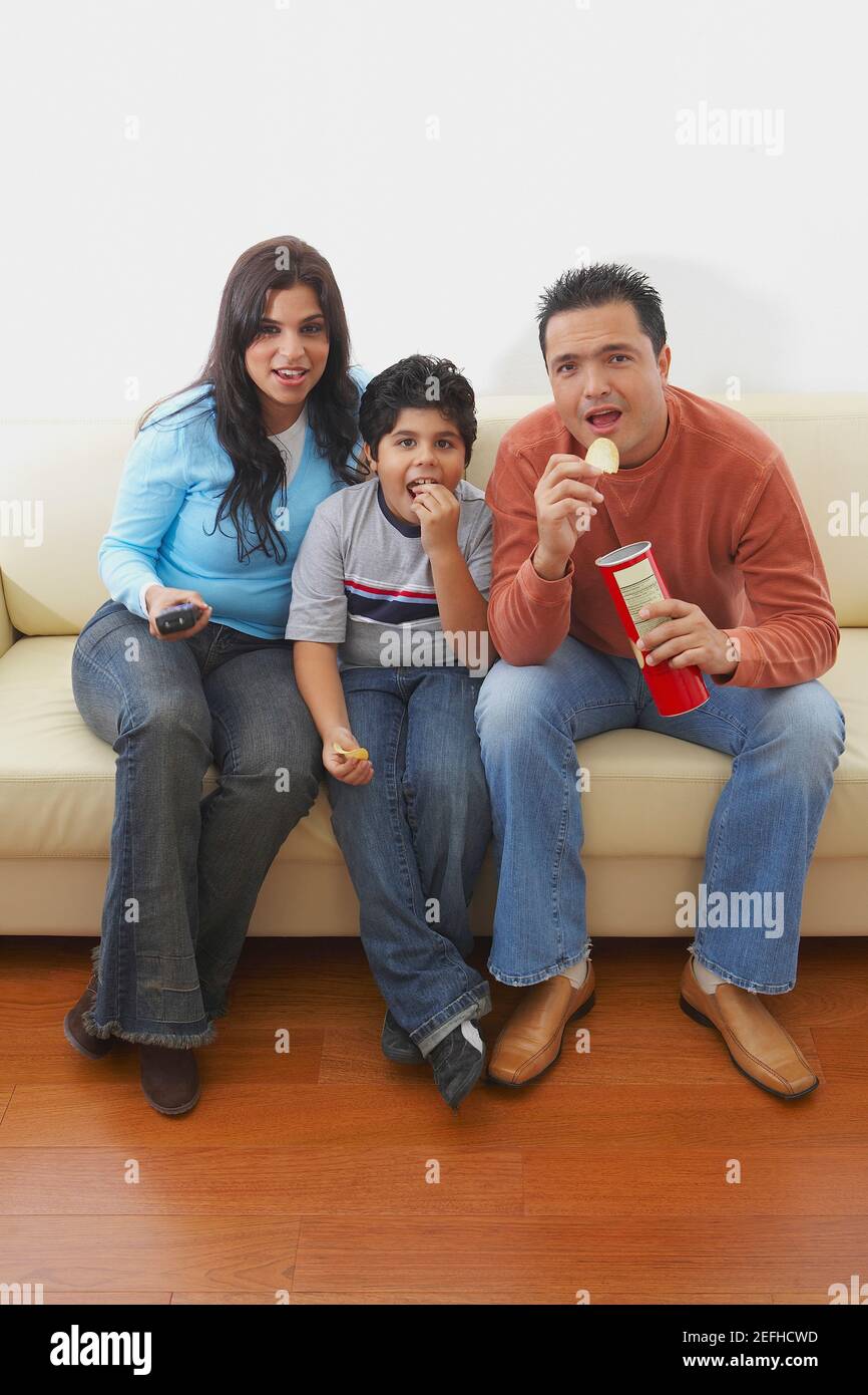 Mid adult man and a young woman sitting with their son on a couch and ...