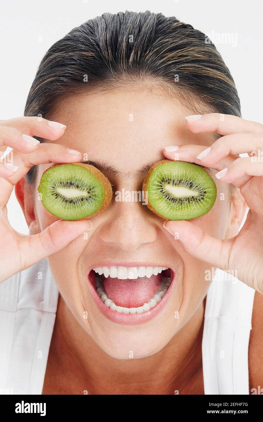 Close up of a young woman holding slices of kiwi fruit in front of her ...