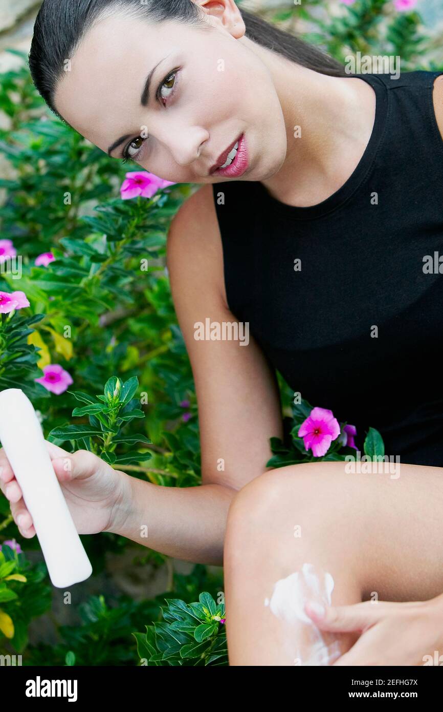 Portrait of a young woman applying moisturizer on her leg Stock Photo