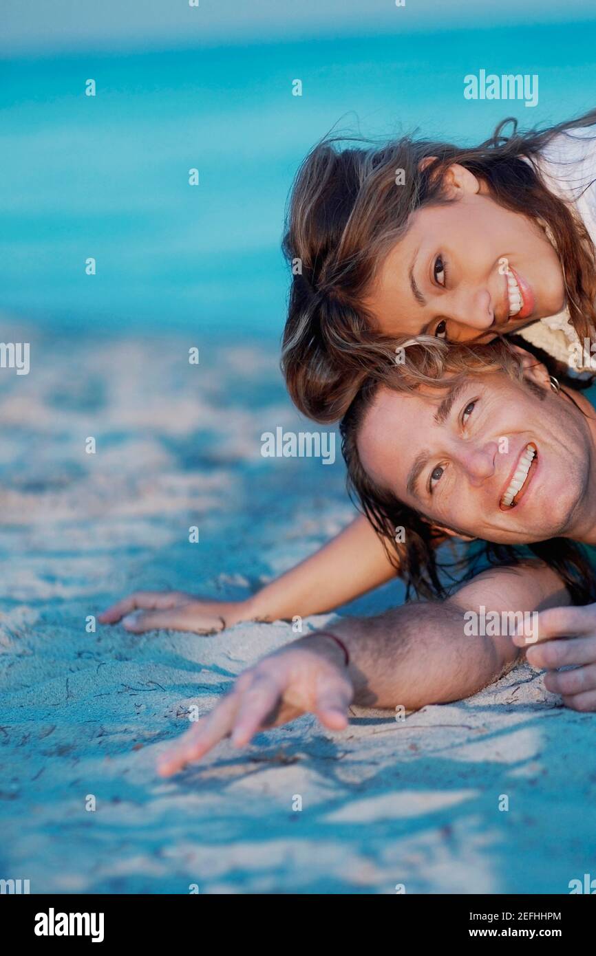 Portrait of a young woman lying on top of a mid adult man on the beach ...