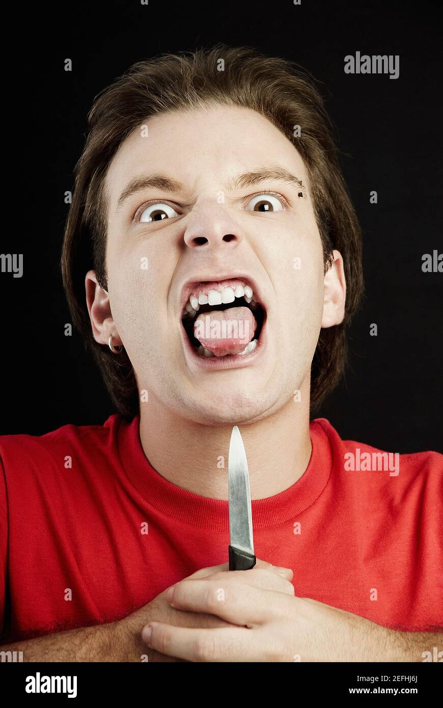 Portrait of a young man holding a knife up to his chin and sticking his  tongue out Stock Photo - Alamy