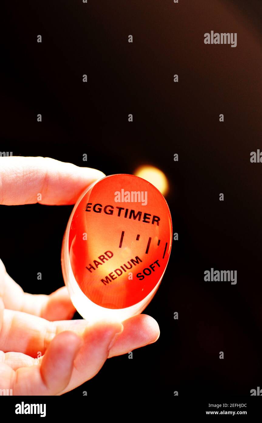 Red plastic egg timer held in white hand, on black background and back lighted. Used for hard, soft or medium boiled egg Stock Photo