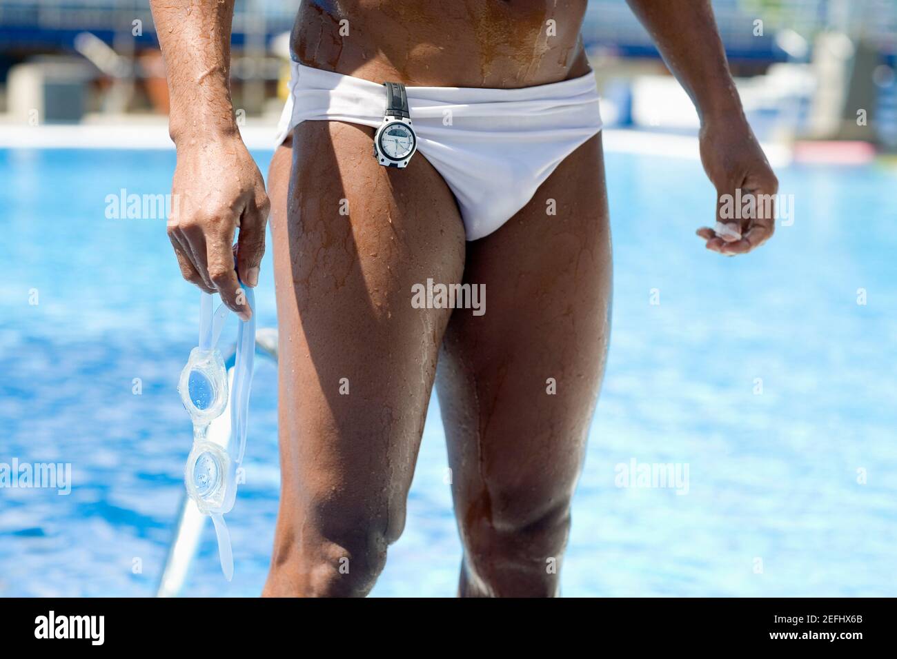 Mid section view of a man holding swimming goggles and standing at the poolside Stock Photo