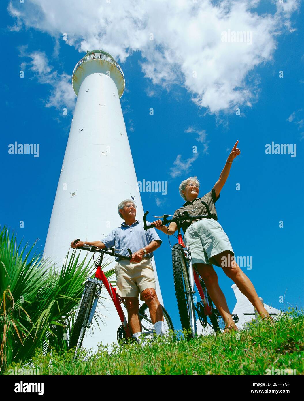 Low angle view of a senior couple standing in front of a tower with their bicycles, Bermuda Stock Photo