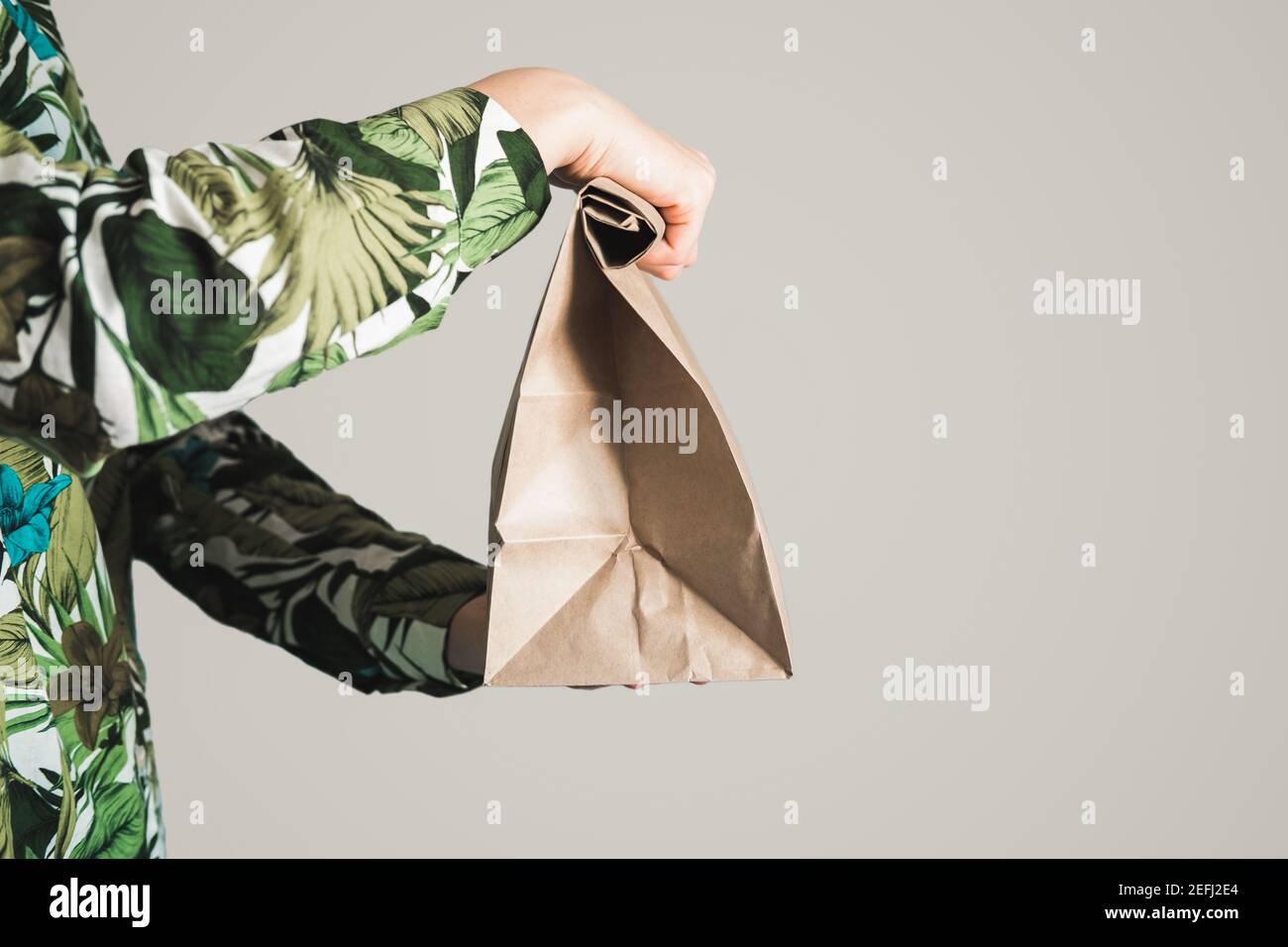 Female hand holds a paper bag against gray backdrop. Empty eco friendly package, gift, surprise or delivery concept Stock Photo