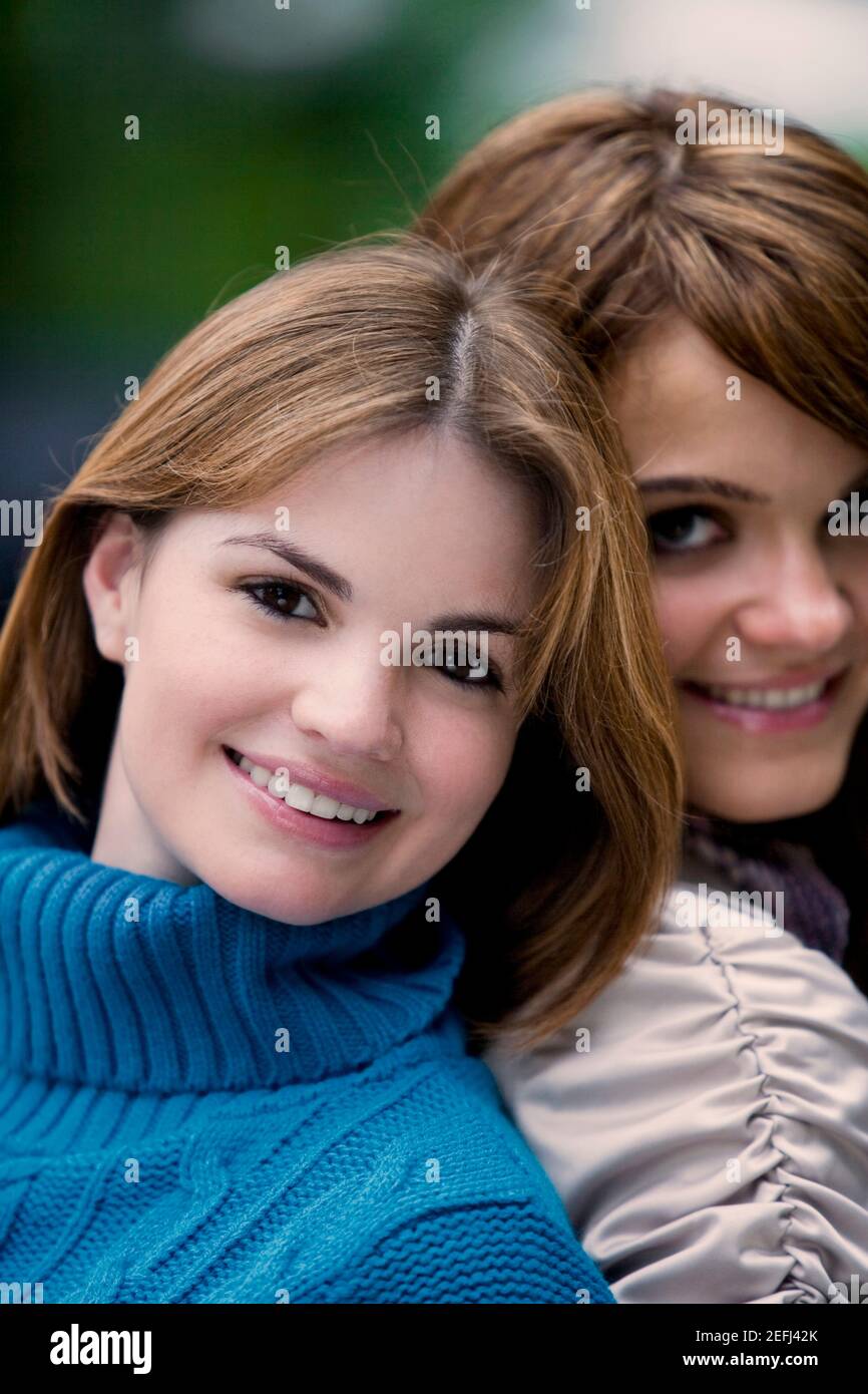 Portrait of two young women back to back and smiling Stock Photo - Alamy