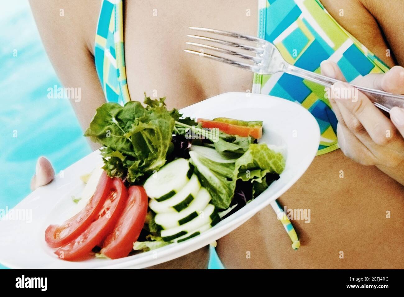 Mid section view of a woman holding a plate of vegetable salad and fork Stock Photo