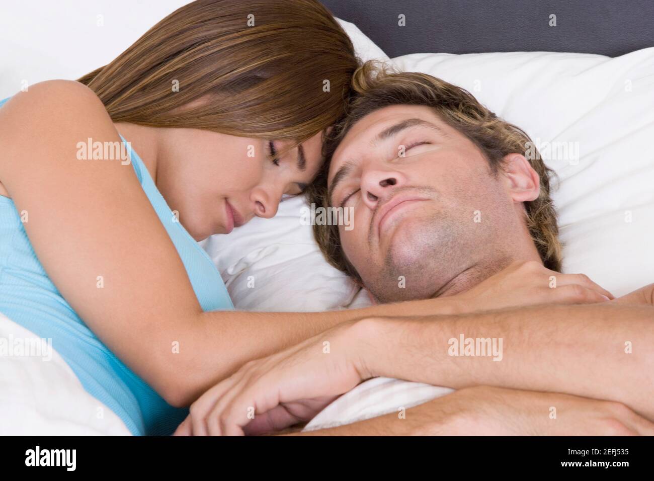 Close-up of a mid adult man sleeping on the bed with a young woman ...