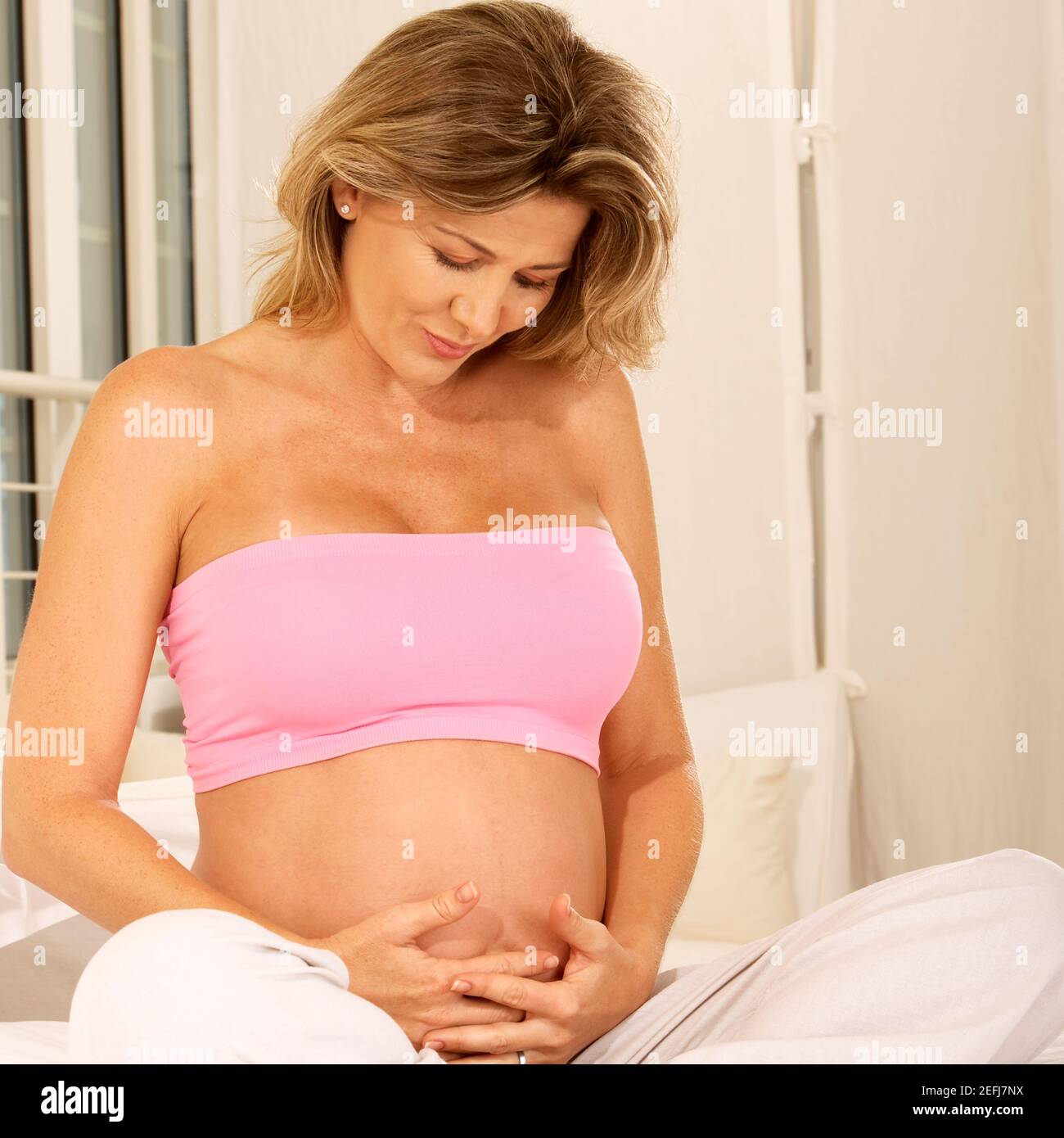 Pregnant woman sitting on the bed touching her abdomen Stock Photo