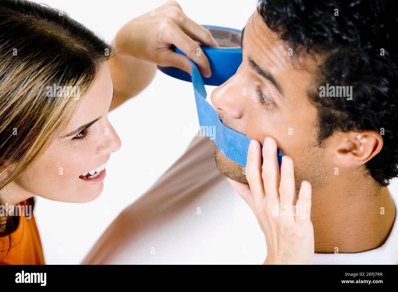 Close-up of a mid adult woman sticking an adhesive tape on a young manÅ½s mouth Stock Photo
