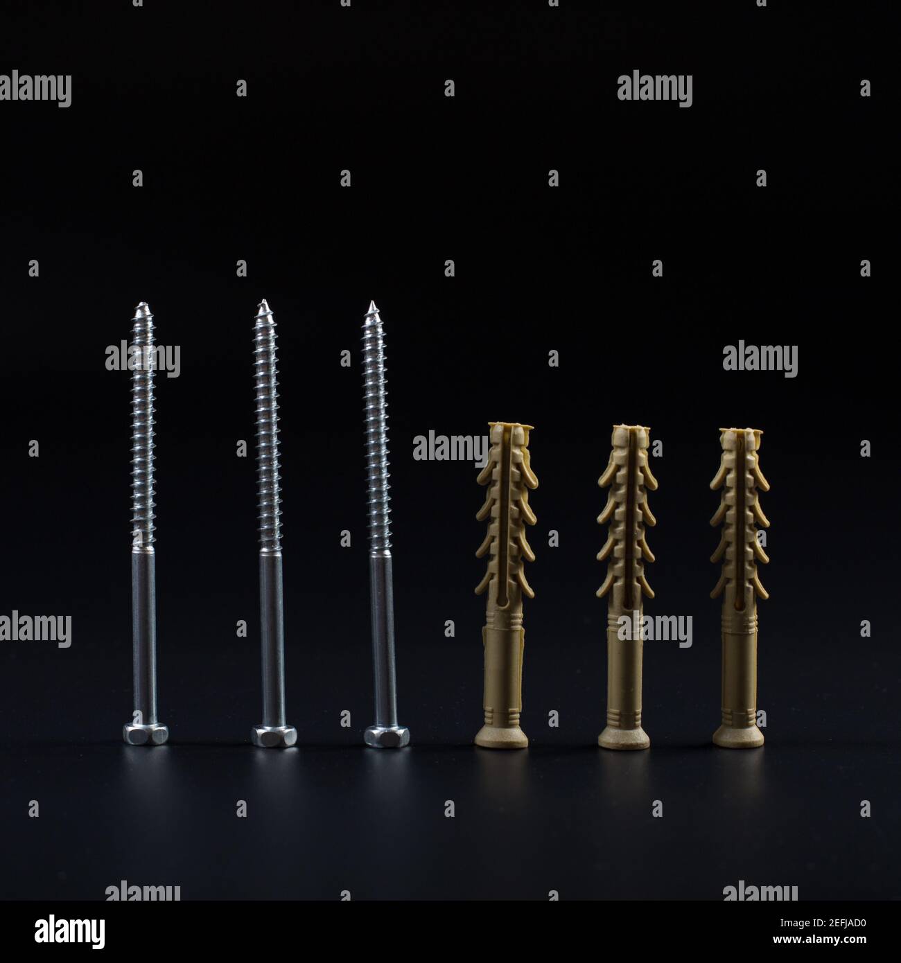 Long plastic dowels with self-tapping screws on a black background. Stock Photo