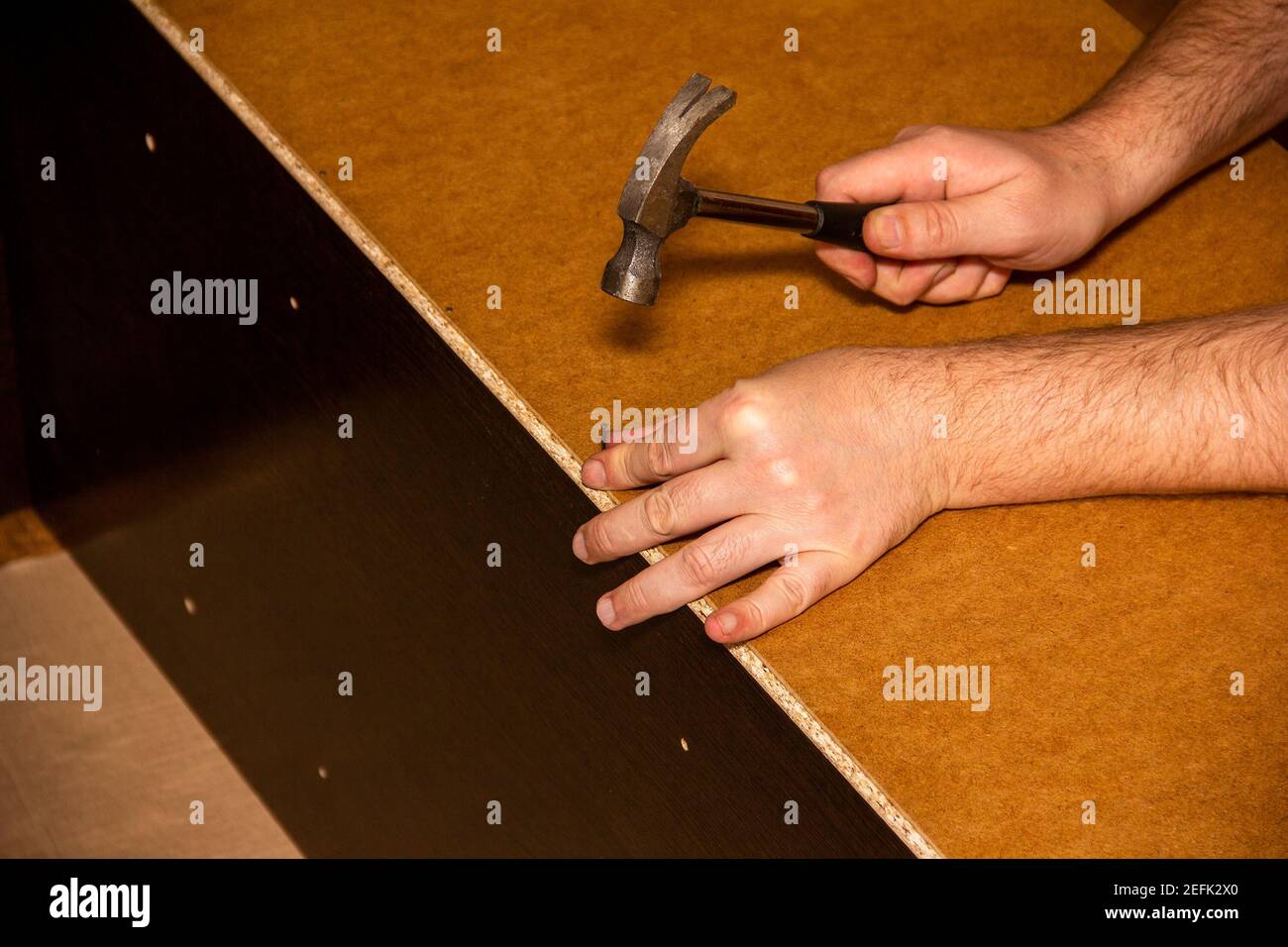 a carpenter furniture maker hammers a nail into the back of the