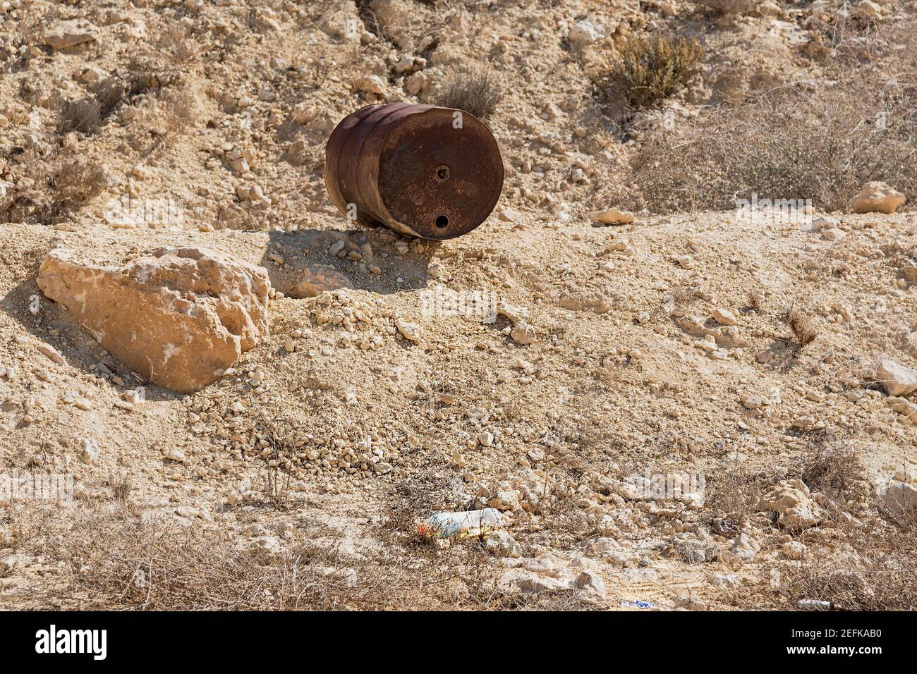 a rusty antique oil barrel sits on a man-made berm above a discarded plastic bottle and bits of trash spoil the view in a nature reserve in the negev Stock Photo