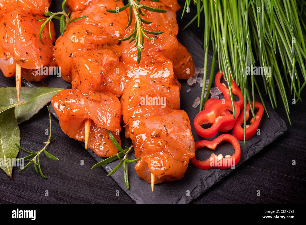 Chicken pieces of kebabs marinated in a red marinade with spices on a dark culinary board,on a background with pieces of pepper. Raw chicken pieces on Stock Photo