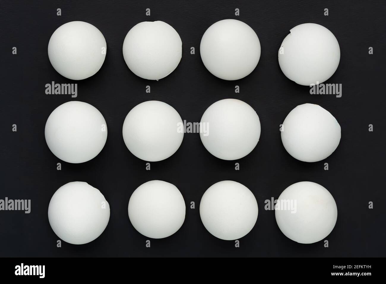 White eggshells are laid out in even rows on a black background. The concept of sameness, equality and equity. The concept of impersonal, stereotyped Stock Photo