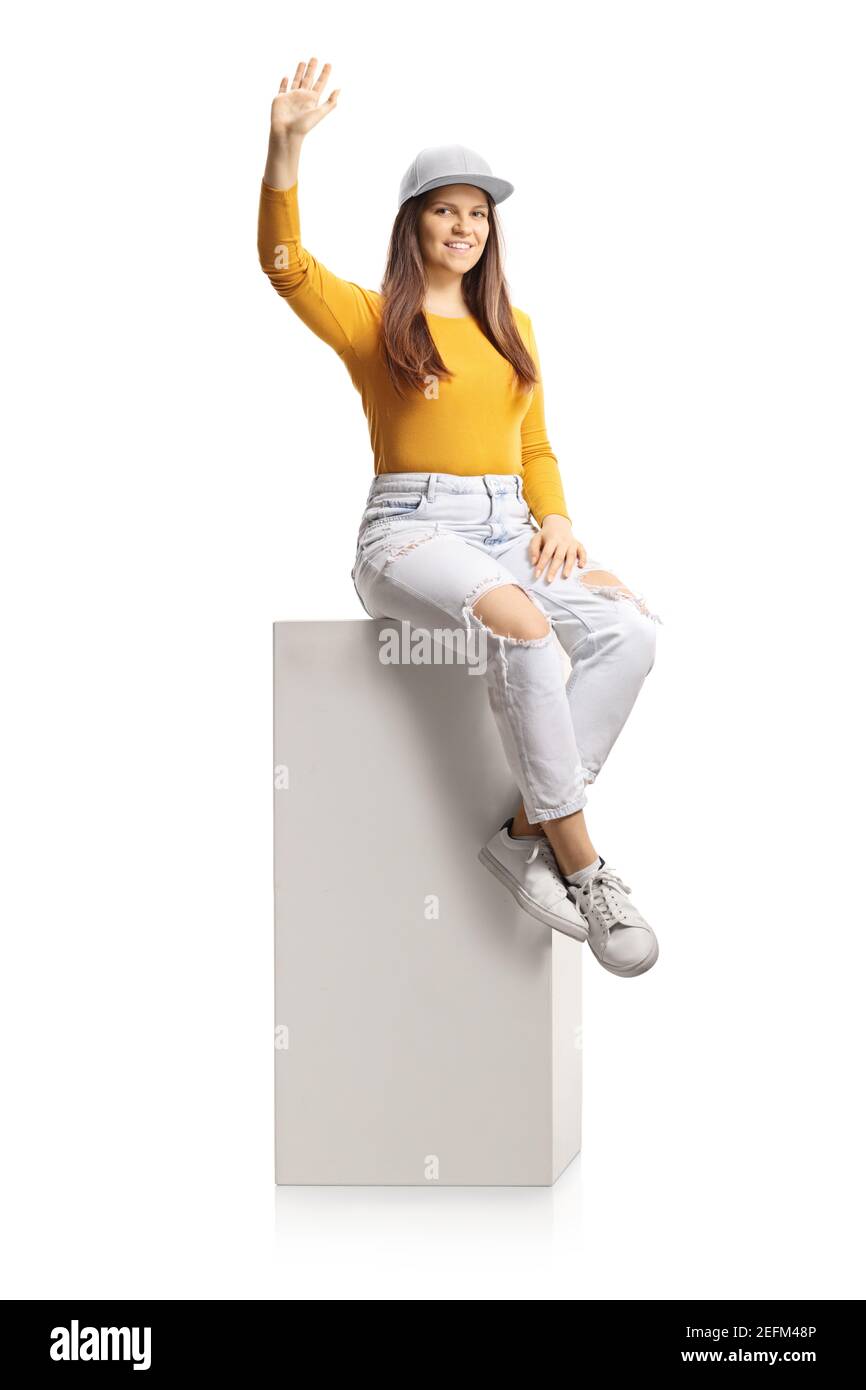 Young female sitting on a column and waving at camera isolated on white background Stock Photo