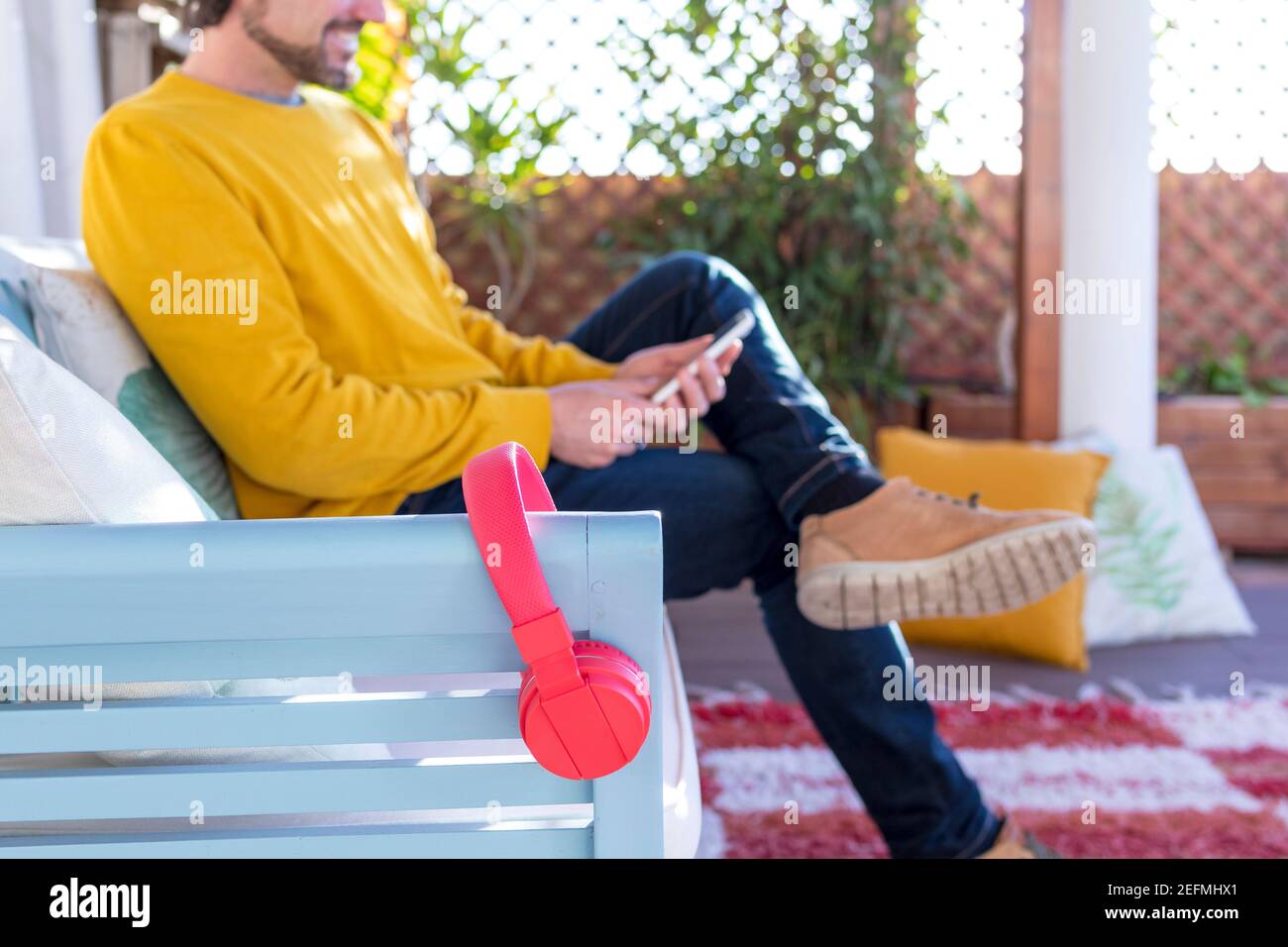 Unfocus and unrecognizable man chatting on his smartphone. Red headphones on foreground. Focus on red headphones. Selected focus. Stock Photo