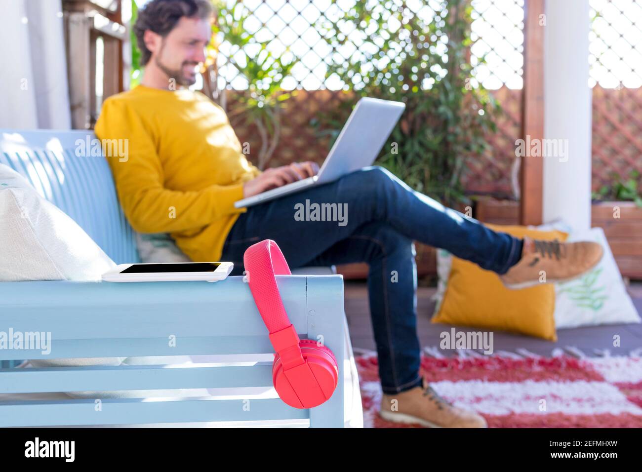 Unfocus and unrecognizable man on background working on his laptop. Red headphones on focus on foreground. Selected focus. Stock Photo